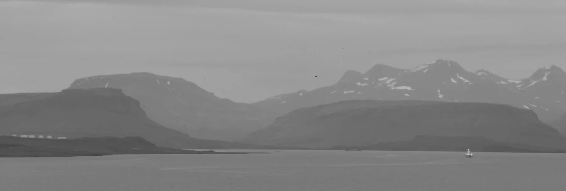 Hvalfjörður under an overcast sky — mountains in mist, and a ship small on the grey water